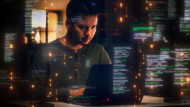 Focused young male developer working on a laptop at night surrounded by floating digital code and binary data holographic interface in a dark room office setting. Software technology development.
