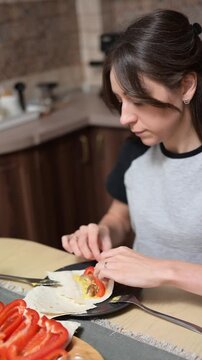 Young woman eating tortilla wrap and vegetables at kitchen table vertical video footage