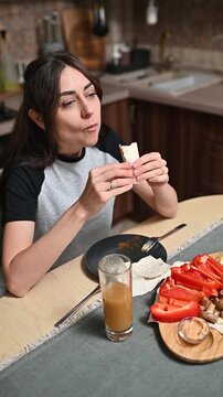 Woman eating flatbread wrap at kitchen table vertical footage