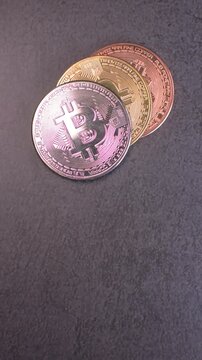 Vertical video of stacked bitcoin cryptocurrency coins with copper, gold, and silver finishes placed on a gray granite surface while moving light creates reflective metallic highlights, symbolizing bl