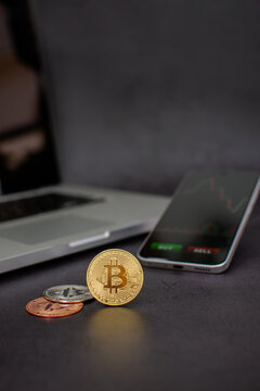 Vertical golden bitcoin coin with market chart and laptop background