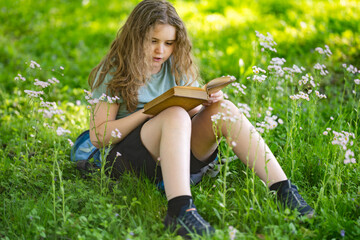 Fototapeta premium Child reading book in summer park. Focused child enjoys reading book outdoors. Peaceful learning follows child reading book. Vintage story creates calm reading book.