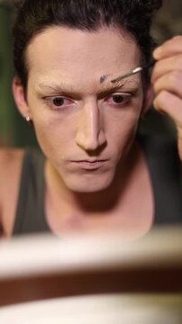 Concentrated man applying theatrical makeup on his face, creating a dramatic look for a performance