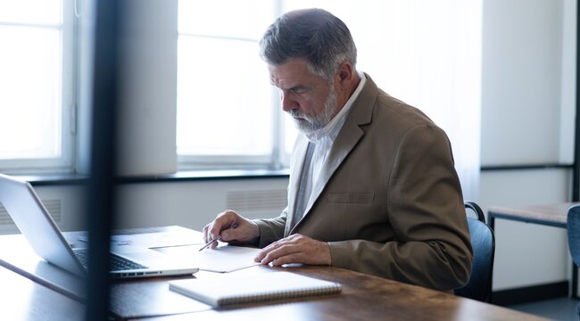 Mature businessman working with document in modern office, reading contract, analyzes graph