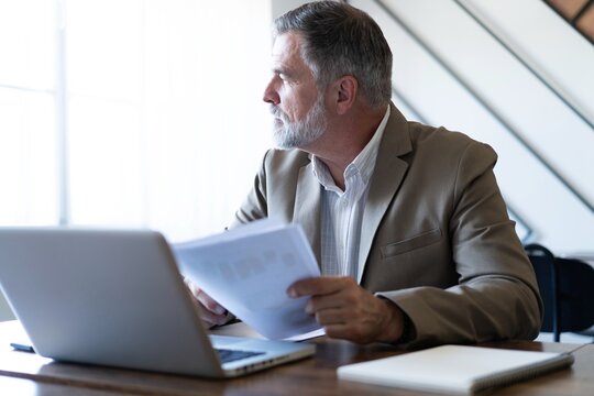 Mature businessman working with document in modern office, reading contract, analyzes graph