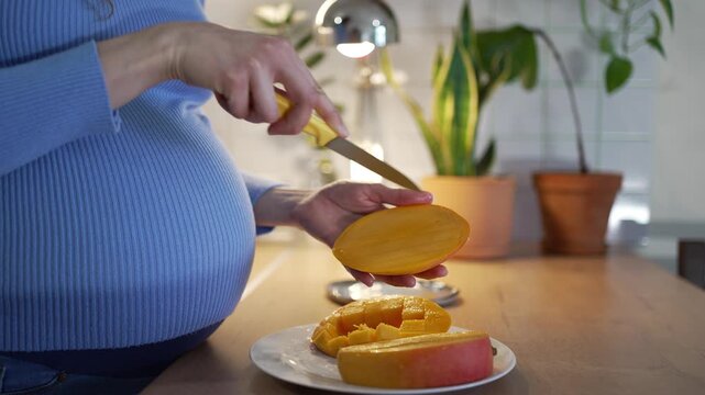 Pregnant woman in her third trimester slicing a ripe mango in the kitchen, emphasizing a healthy diet rich in vitamins for her unborn baby's well-being and a joyful motherhood journey