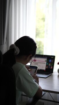 Cinematic wide over the shoulder shot of a young female professional with glasses holding a digital tablet and working on laptop at bright desk setup