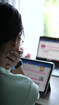 Cinematic wide over the shoulder shot of a young female professional with glasses holding a digital tablet and working on laptop at bright desk setup
