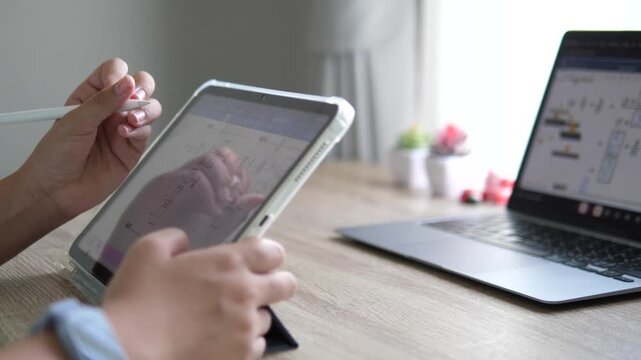 Cinematic close-up of a professional's hands using touch gestures on digital tablet screen while holding a stylus pen, blurred laptop background