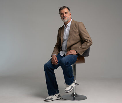 full body picture of happy elegant mature man sitting, laughing in front of white
