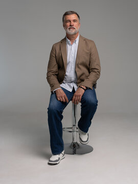 full body picture of happy elegant mature man sitting, laughing in front of white