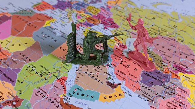 A toy soldier is dropped onto a map facing Iran and the Strait of Hormuz. Visual metaphor for a sudden military escalation, boots on the ground and regional standoff.