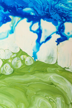 Swirling patterns of blue and green paint on a canvas create an abstract design