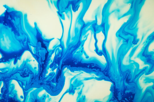 Swirls of blue paint mixing on a white surface in an art project setting