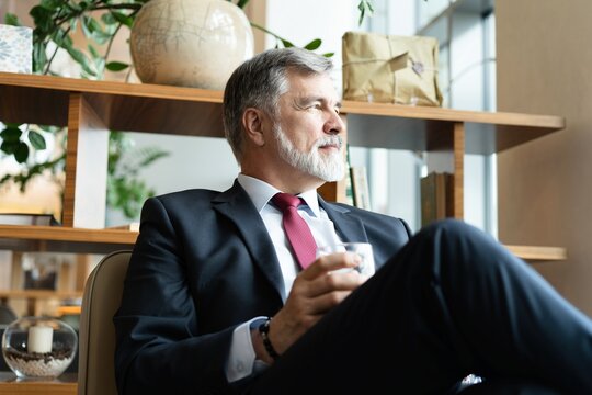 Mature bearded businessman in formal wear drinking fresh water while sitting in the modern office
