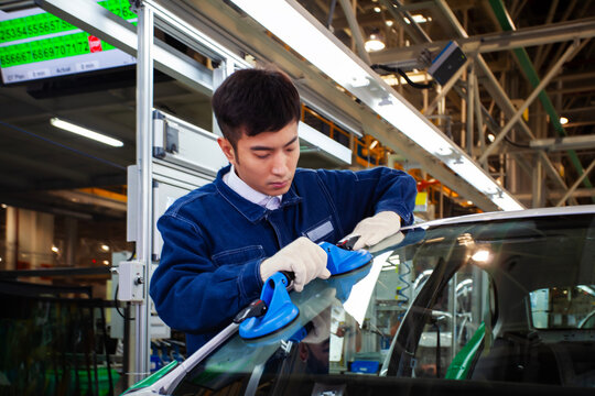 Asian workers at a car factory are installing car windows.