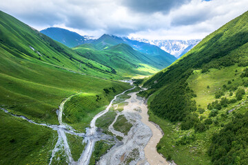 Fototapeta premium Svaneti Georgia mountain valley with river road, green Caucasus hills, dramatic clouds, wilderness travel and hiking destination.