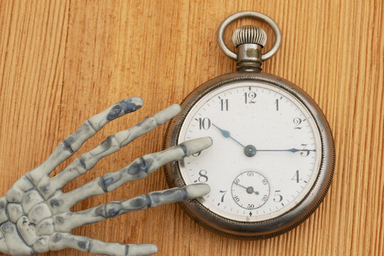 Skelton hand with an antique pocket watch on a wood desk