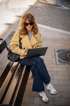Modern mature woman working on laptop on a city bench, digital nomad lifestyle