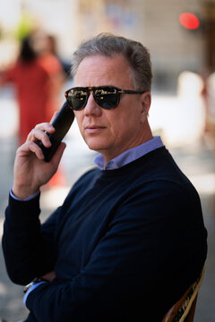 Senior man sitting at table at sidewalk cafe and using a cellphone