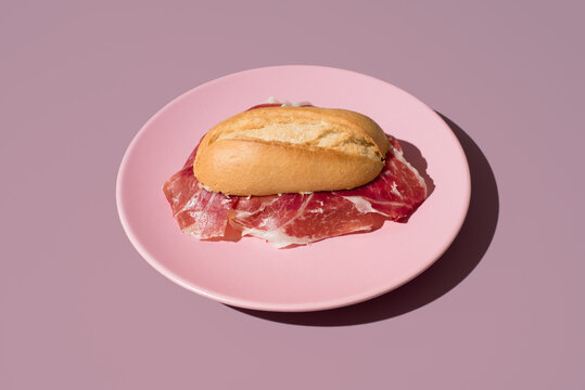 Delicioso bocadillo de Jam&oacute;n curado ib&eacute;rico de bellota en un plato rosa sobre fondo rosa