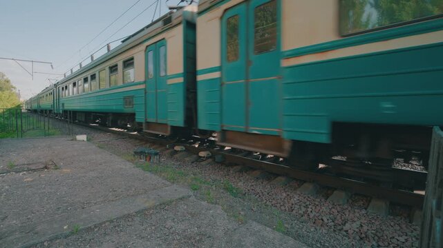 Low-Angle Side View: Passenger Commuter Train Moving Along Railroad Tracks in Slow Motion | Teal Vintage Rail Cars Passing by with Motion Blur | Suburban Railway Transportation