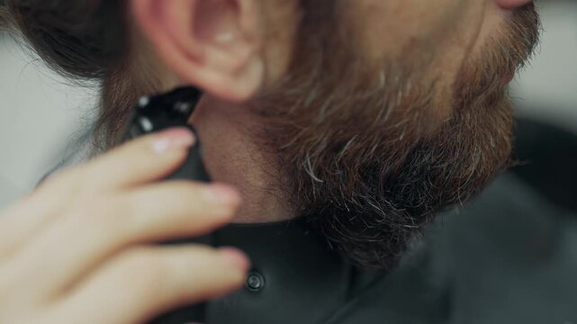 Close up of barber trimming neck hair with electric clipper during beard grooming procedure in modern barbershop