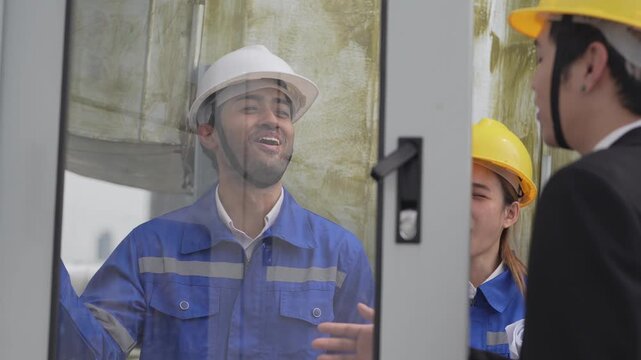 A mechanical site engineer in a blue uniform and hardhat adjusting control panel parameters while a green building consultant tracks progress during an outdoor system audit.