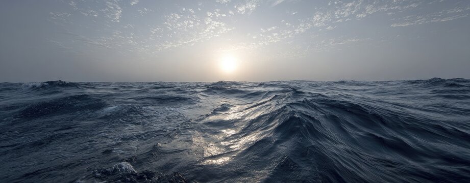 Expansive ocean waves under a hazy, pale sun with a few scattered clouds