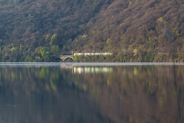 Fototapeta premium Train crossing old bridge over calm lake water
