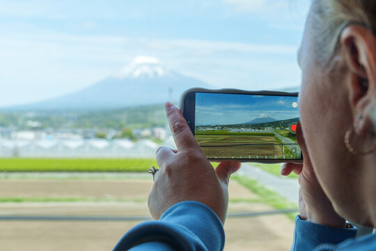 Woman uses a phone to take photos of Mt. Fuji while on the bullet train in Japan