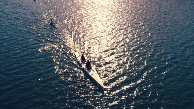 Drone shot of kayakers and rowers moving across sunlit lake water with bright reflections and ripples. Scenic outdoor sport scene showing teamwork, training, freedom and nature.