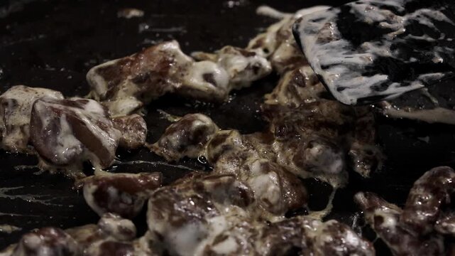 Cooking process of meat pieces being sauteed in a frying pan with a spatula, showcasing gradual browning and caramelization in a kitchen setting
