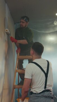 Men painting interior, Men meticulously painting textured wall inside building with safety gear and proper tools