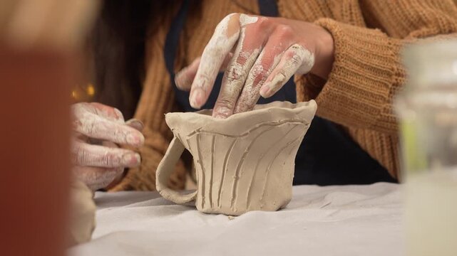 Caucasian woman potter craftsman decorating pottery vase sculpt dishware in pottery workshop.