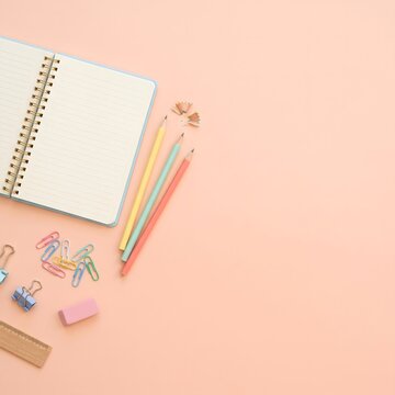 Aesthetic flat lay of open notebook and stationery on pastel peach background