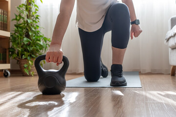 Mature woman in activewear doing a kneeling kettlebell lunge in her living room, maintaining strength training and a healthy, sustainable fitness routine for wellness and mobility