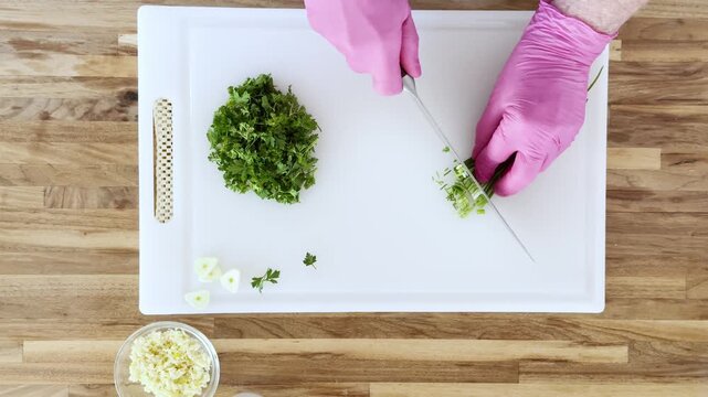 Top‑down view of hands cutting fresh herbs such as chives and parsley on a chopping board.