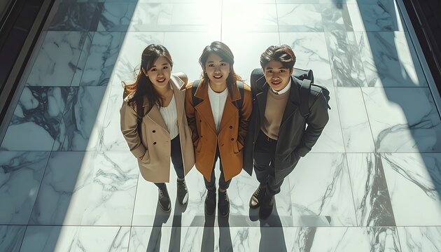 Three young business professionals looking up with smiles in a modern office lobby, bright sunlight casting long shadows on the marble floor, teamwork and success concept