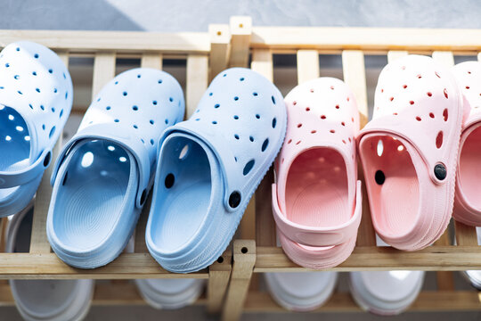 Comfortable perforated plastic clogs displaying pastel colors on a wooden shoe rack, representing footwear fashion and storage