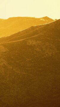 The sun sets over a mountain landscape. Trails appear on the surface, and the light gives a yellow hue to the scene. The terrain shows rocky and uneven features.