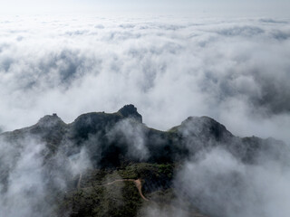 Fototapeta premium Mountain peaks surrounded by sea of clouds with winding road and rugged terrain