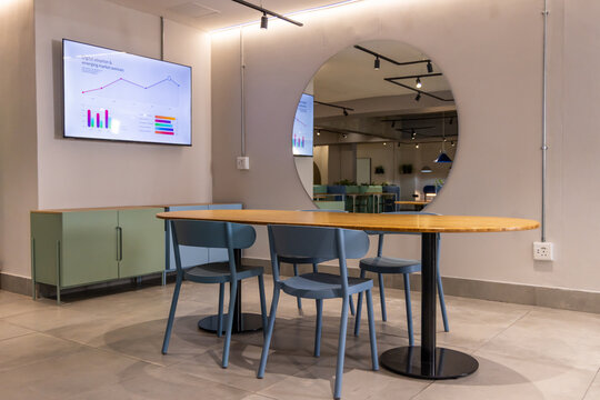 Oval table on black pedestals occupying lounge center, showing blue molded chairs, mirror, monitor