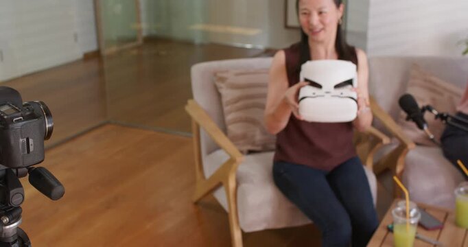 Diverse female coworkers, presenter demonstrating white headset in home studio while camera filming