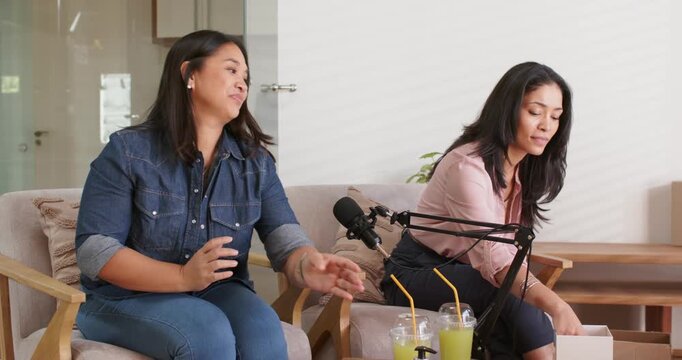 Diverse women hosts adjusting boom mic opening box greeting new cohost entering studio for podcast