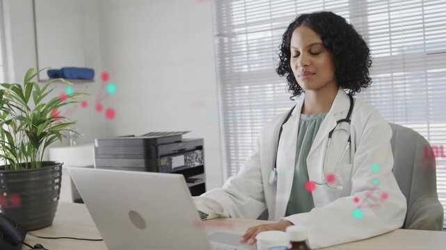 Female physician typing on laptop in clinic, causing animated red teal dots while reviewing data