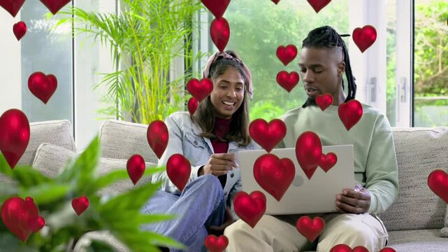 Woman tapping card and pointing at laptop beside man, red hearts circling subjects, tech demo