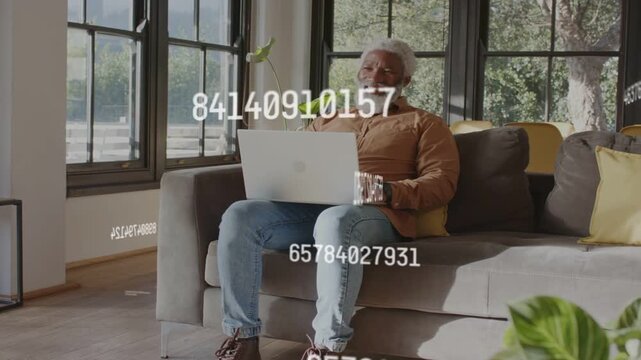 Senior man sitting on sofa typing on laptop, starting moving numeric overlays and reviewing finance