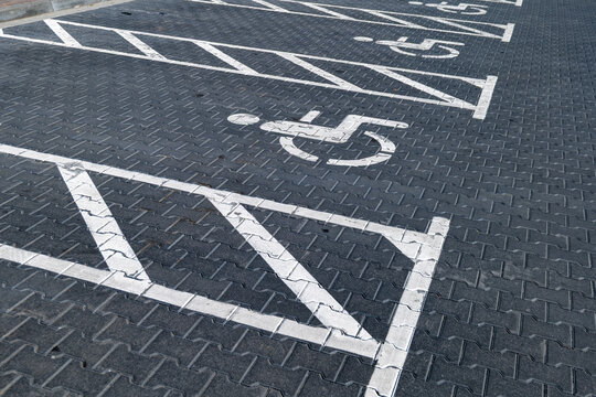 Parked cars in a public lot show clear parking markings for disabled drivers on the ground in bright daylight