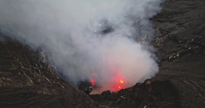 Mount Yasur volcano crater on Tanna Island in Vanuatu erupting with incandescent molten lava and thick white smoke billowing from the active vent, showing powerful geological forces. Drone footage